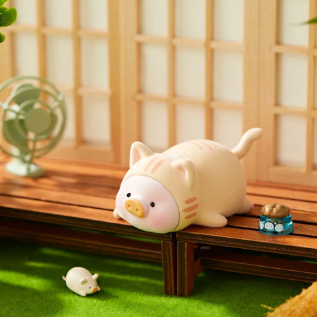 LuLu the Piggy figurine dressed in cat costume lying on wooden porch near mouse toy and food bowl on green grass