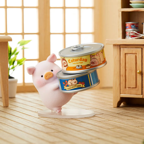 LuLu the Piggy figurine holding two illustrated cat-themed tin cans in a cozy room with wooden floor and furniture