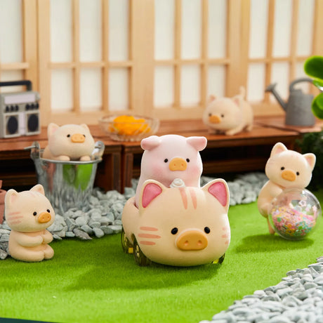 LuLu the Piggy figurine in a cat costume riding a small pig-shaped toy with other pig and cat figures nearby on grass