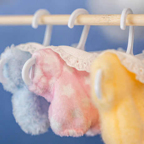 Soft plush pajamas in pastel blue, pink, and yellow with lace collars hanging on white hangers against blue background