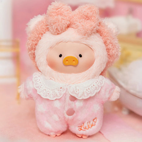 Soft LuLu Piggy plush doll wearing pink heart pajamas with lace collar and fluffy hood in cozy bedroom setting