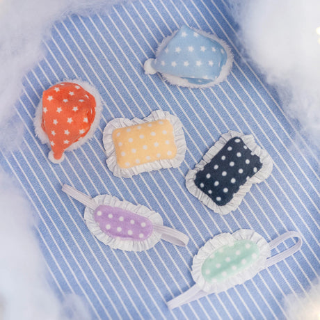 Colorful polka dot plush sleep masks and caps with ruffled edges arranged on striped blue fabric background