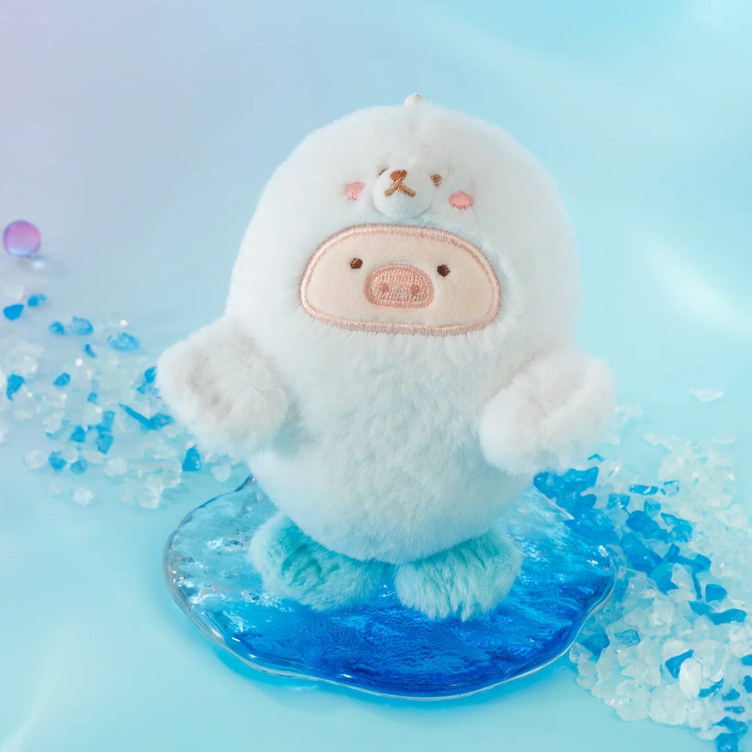 The LuLu The Piggy - Baby Seal LuLu Plush Keychain features a round, white seal with a bear face and pink cheeks standing on blue ice, making it the perfect cute keychain for any ocean-themed adventure.
