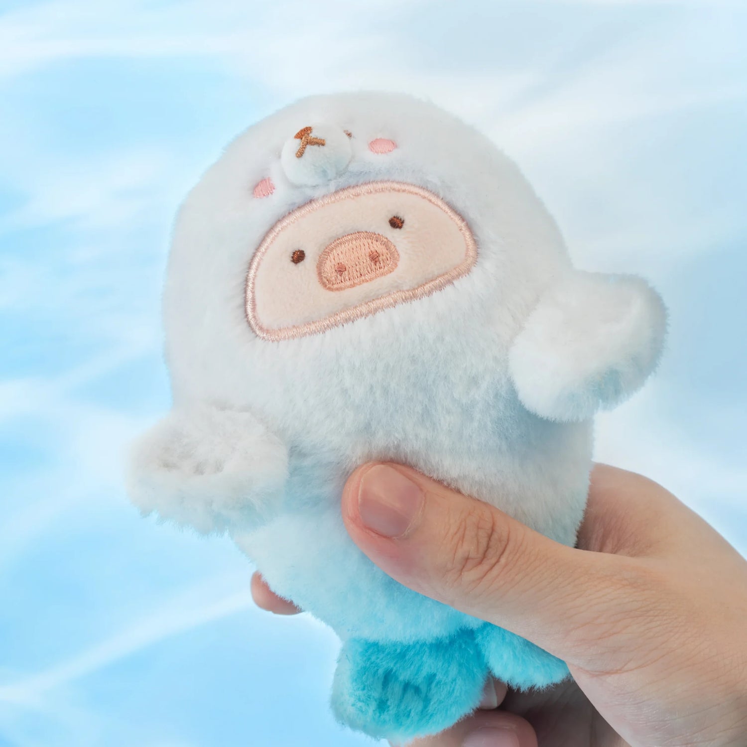 A hand holds a LuLu the Piggy - Baby Seal LuLu Plush Keychain, featuring embroidered light blue and white seal details—cute and portable from LuLu The Piggy, perfect for ocean-themed adventures on the go.