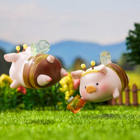 Two LuLu the Piggy figurines dressed as bees flying over grass, one holding a honey jar with blurred garden background