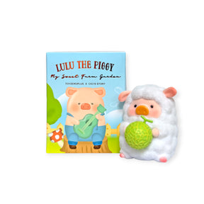 LuLu the Piggy figurine dressed as a sheep holding a green vegetable next to a colorful product box