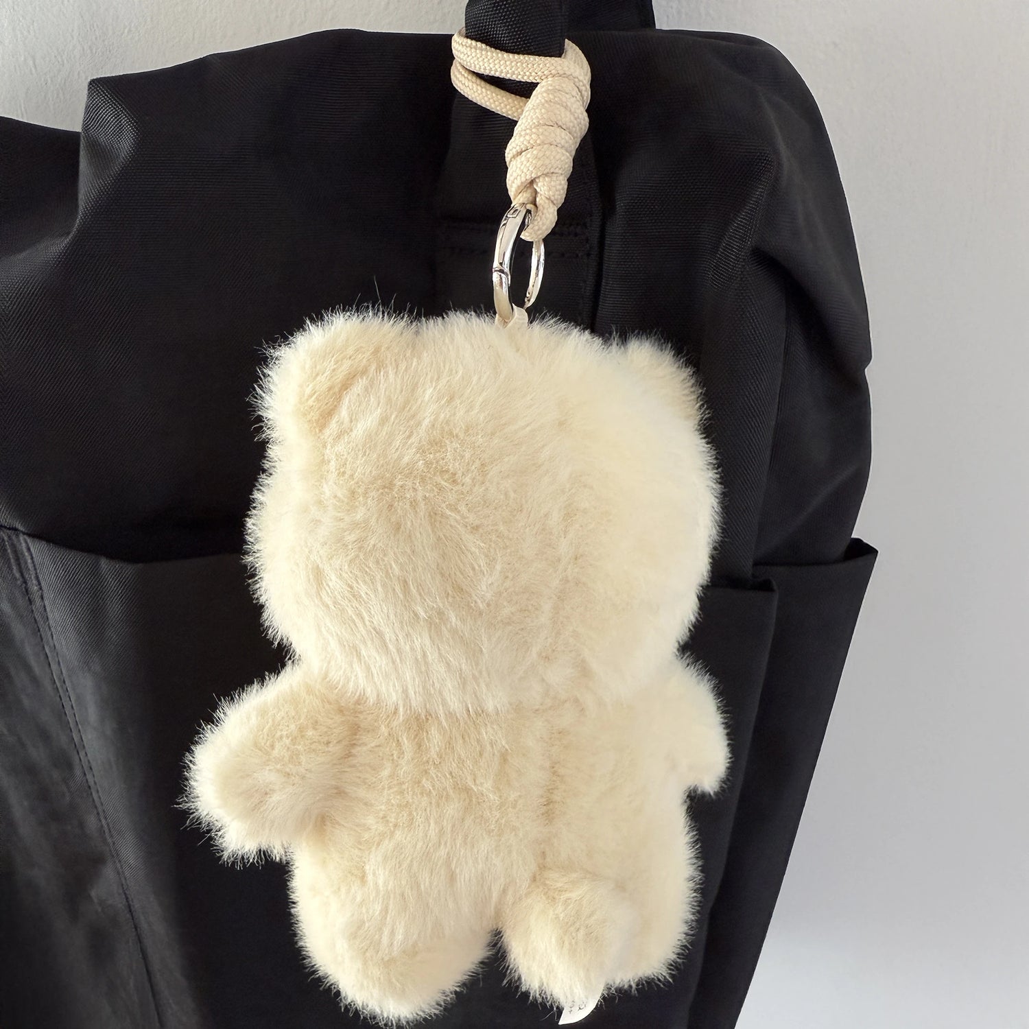 A Teddy LuLu the Piggy Plush Pal - Blind Box by LuLu The Piggy hangs from a loop attached to a black backpack.