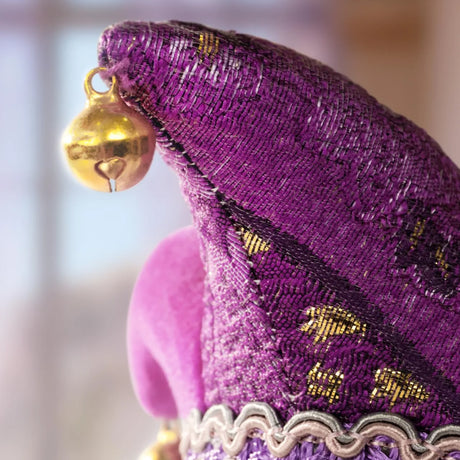 Close-up of purple jester hat with gold bell and silver trim on textured fabric background