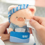 Light pink pig plush keychain with blue striped cap and monitor pouch, held by hand
