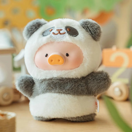 A LuLu The Piggy - Animal Party Puppet Keychain Blind Box plush pig in a panda costume stands among wooden toys and soft colors—a must-have for fans of LuLu The Piggy and cute collectible plush figures.