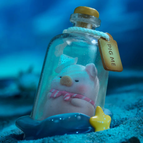 A small LuLu The Piggy figurine with a pink bow sits inside a "PIG ME" glass bottle on sand, atop a blue whale base with a yellow starfish—an Ocean Blind Box collectible perfect for fans of LuLu The Piggy.