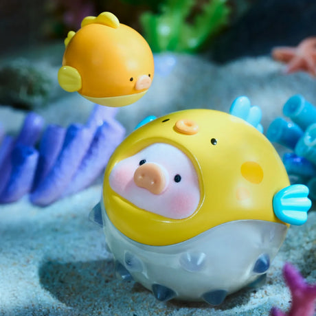 Two round, yellow, fish-like figures from the LuLu The Piggy - Ocean Blind Box by LuLu The Piggy rest on sand with purple coral; one is small and floating, the other is larger with a pig-like face and blue fins.