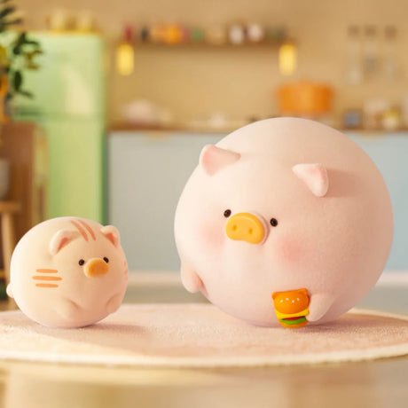 Two pastel animal figurines—a LuLu The Piggy holding a burger and a cat—sit on a mat in a cozy kitchen, perfect for fans of the LuLu the Piggy - Stay With You Blind Box by LuLu The Piggy.