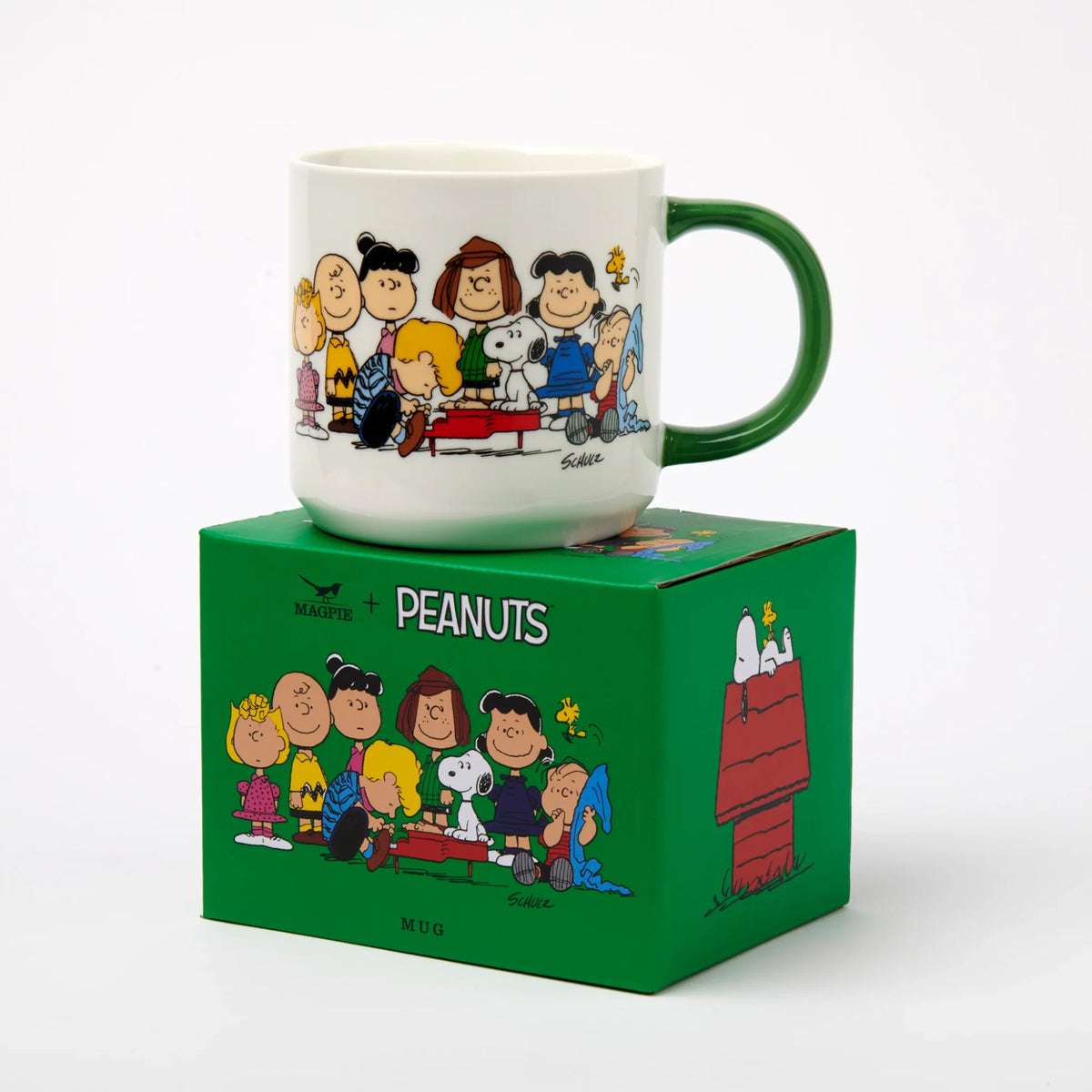 White ceramic Snoopy mug with Peanuts characters and green handle, shown on box