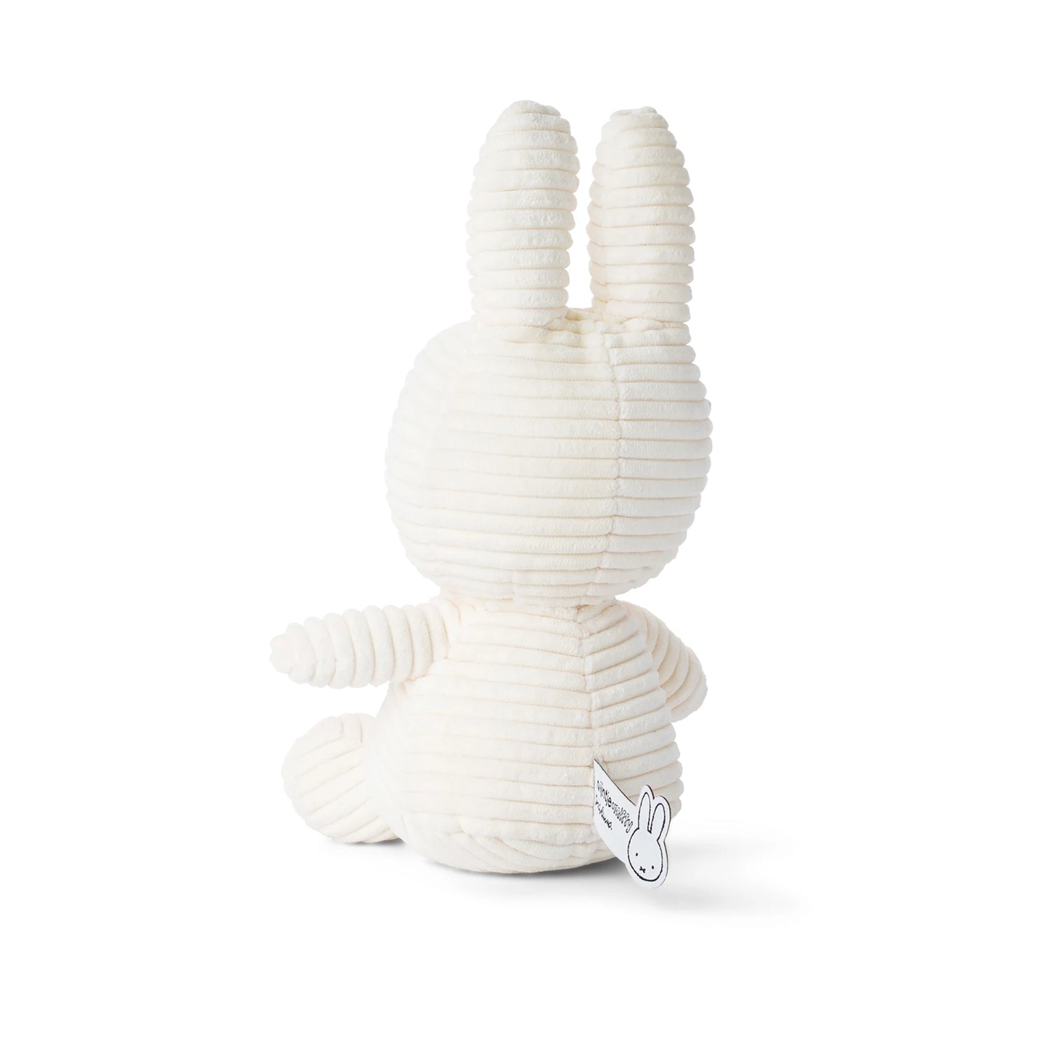The Miffy Bunny Plush Corduroy in white, standing at 23cm, sits peacefully with its back turned and a tag gently attached to its left side. Crafted by the Miffy brand from baby-safe materials, this cozy companion features a charming corduroy texture, making it ideal for little ones.