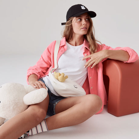 Woman in pink shirt wearing black Miffy Bunny Cap with white embroidered face sitting next to plush toy and bag gallery position 1