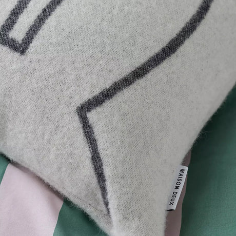 Light gray wool cushion cover with black outline detail and stitched brand label