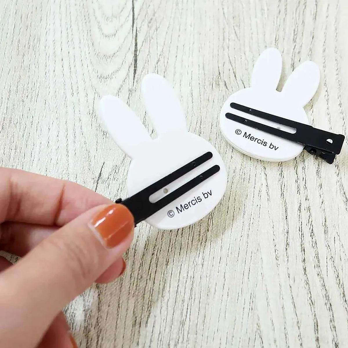 White bunny hair clips with black snap barrettes, held in a hand