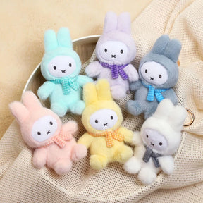 Five pastel-colored Miffy plush keychains wearing checkered scarves arranged on beige fabric background