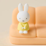 Phone stand sofa with white rabbit figure in yellow outfit on peach seat