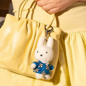 A person in a yellow outfit holds a yellow handbag featuring the Miffy Plush Keychain - Daisy Dress by Miffy, attached to the handle.