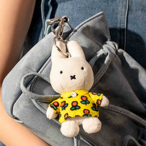 Soft white Miffy plush keychain wearing a yellow dress with colorful tulips attached to a grey bag, gallery image one