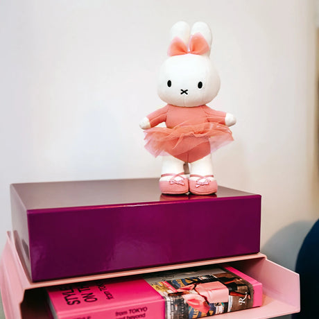 A limited edition Miffy Flower Dress Plush, 23cm, sits on pink and purple boxes next to a rolled magazine.