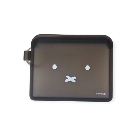 The Miffy Bunny Card Case - Black, by Miffy, is a black rectangular coin purse crafted from durable silicone, featuring a minimalist face design with two white dot eyes and a cross-shaped mouth.