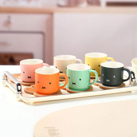 Celebrate Miffy’s 70th with the Miffy 70th Bday Collectible Mug & Coaster Blind Box—six colorful mugs, each with a simple face design, arranged on a tray in a kitchen setting.