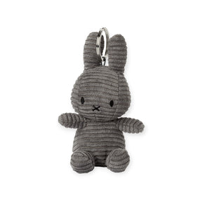 The eco-friendly Miffy Keychain Corduroy 10cm from Miffy showcases a grey fabric bunny with black stitched eyes and mouth, detailed with horizontal corduroy lines, and comes with an attached metal ring.