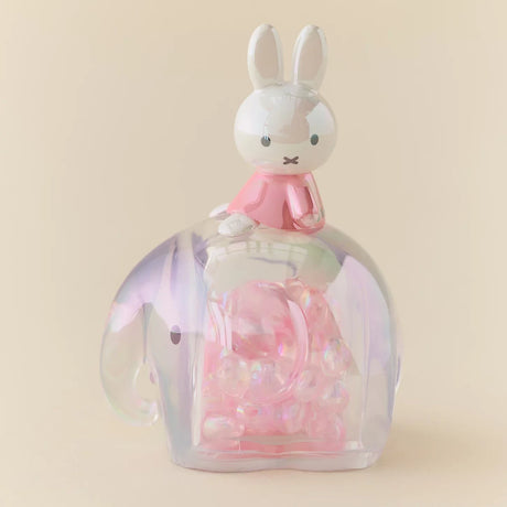 Glossy Miffy figure in pink atop a translucent elephant snowglobe filled with shimmering iridescent beads on beige backdrop