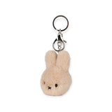 The Miffy Fuzzy Keychain in beige, by Bon Ton Toys, showcases a fluffy bunny head with stitched eyes and nose. Equipped with a metal ring and clasp, it's both charming and crafted from Sustainably Soft materials, ideal for eco-conscious plush fans.