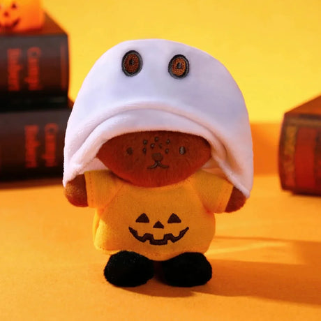 Small plush keychain wearing a yellow pumpkin shirt and a white ghost hood with embroidered eyes on orange background