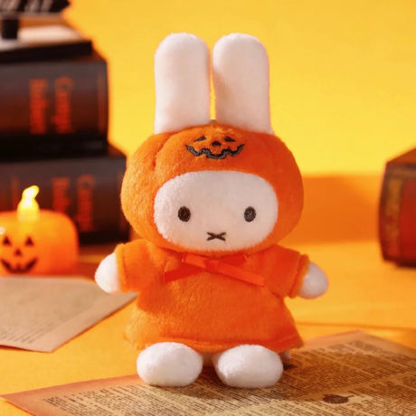 Miffy plush keychain dressed in an orange pumpkin costume with Halloween decorations and books in the background
