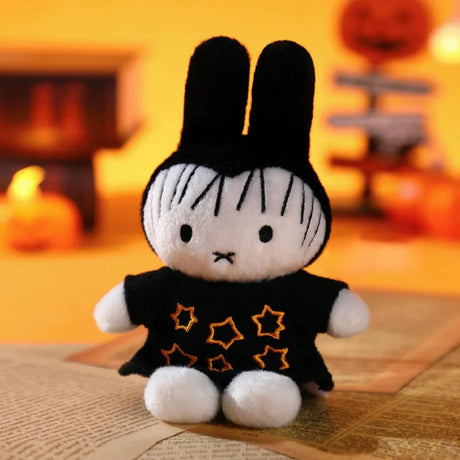 Miffy plush keychain dressed in black star-patterned cape sitting on open book with pumpkin and Halloween decor background