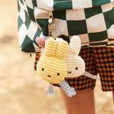 Close-up of a backpack featuring two charming Miffy Plush Flat Keychains in corduroy, one in a delightful yellow and the other in pristine white, both showcasing the stylish design synonymous with Miffy. The checkered pattern adds elegance while upholding an eco-friendly ethic.