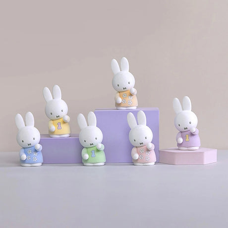 Six Miffy pen tray organisers in pastel outfits holding small objects arranged on purple and pink geometric platforms