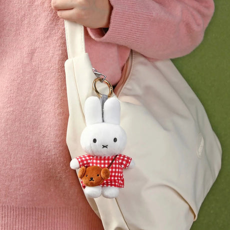 White plush bunny keychain wearing red checkered dress holding small brown bear purse attached to beige bag strap