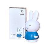 A charming addition to any space, the blue money box featuring a bunny figurine from Miffy stands proudly beside a white box labeled "Atelier Pierre Junior," echoing the iconic Miffy Bunny - Blue Money Box theme with its delightful bunny design. It's perfect for teaching little ones about money management while adding a whimsical touch.