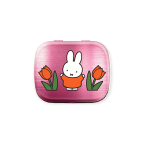The Miffy Pill Tin - Tulips by Miffy is a small pink tin featuring the iconic white rabbit in an orange dress with two red tulips, bringing Dutch floral charm.
