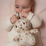 A baby cuddles the Miffy Plush Vintage Flowers All Over - 25cm by Miffy while lying on a light pink surface.