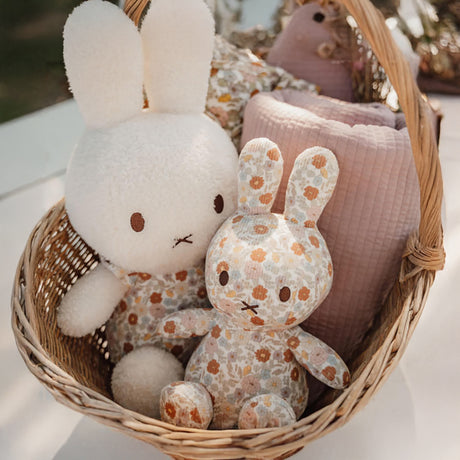 In a woven basket beside a pink quilted blanket, two Miffy Plush White & Vintage Flowers toys, each measuring 35cm and featuring floral patterns reminiscent of Little Dutch designs, are nestled together.