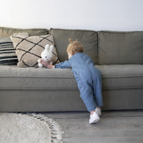 A toddler in a blue jumpsuit eagerly reaches for the Miffy Plush Fluffy Plush Pink - 25cm nestled on a gray sofa.