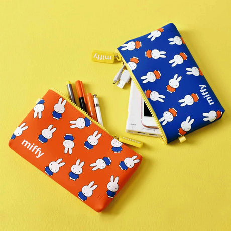 On a yellow surface, two Miffy Bunny Zipper Pouches sit. The orange one holds pens, while the stylish and versatile Miffy Bunny Zipper Pouch 19cm in Blue is partially open to show its contents.