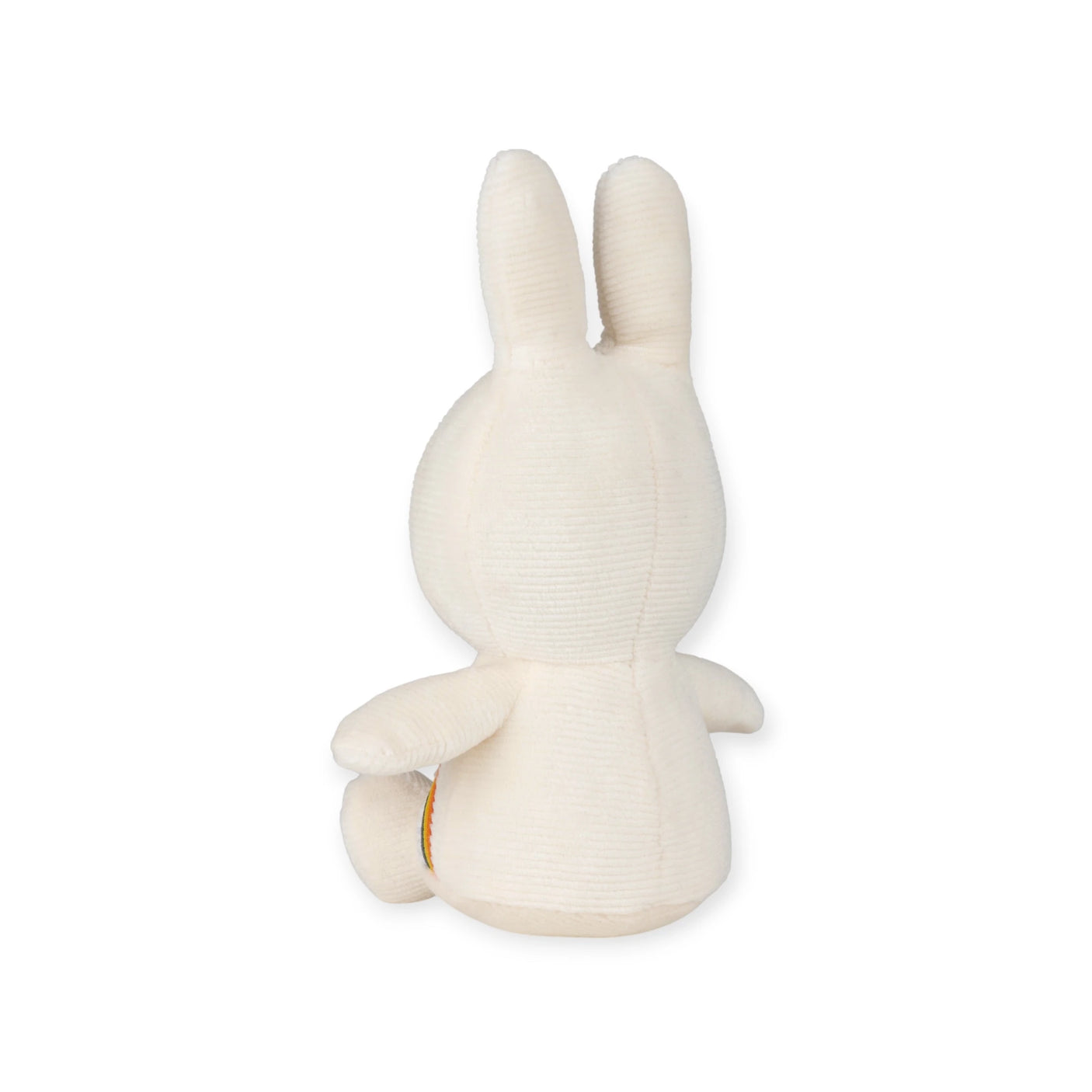 The Miffy Rainbow Plush - 18cm, features a back view of the bunny toy with long ears and a round body. Made by Miffy from super-soft textured fabric, it sits on a white surface highlighting its embroidered rainbow details.