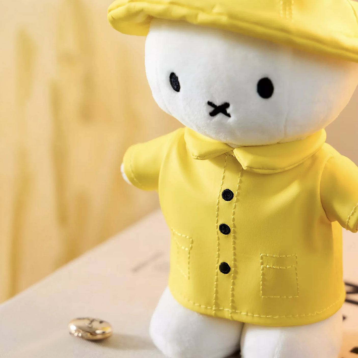 White plush bunny wearing yellow raincoat and matching hat standing on book with blurred background