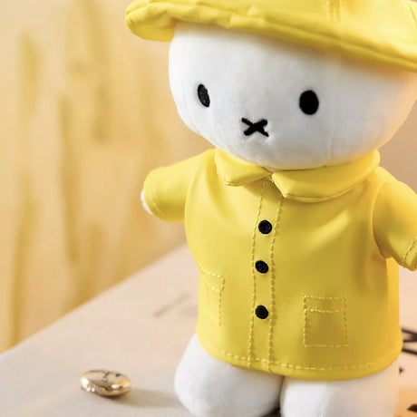 White plush bunny wearing yellow raincoat and matching hat standing on book with blurred background