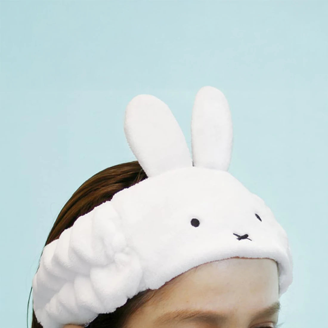 Someone sporting the Miffy Bunny - Spa Headband, with a plush bunny face and ears, poses against a simple light blue background.