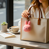 Miffy Squish Ball Keychain - Pink attached to beige handbag held by a woman at a wooden café table by Miffy