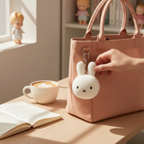 Miffy Squish Ball Keychain - White clipped to a beige bag with hand touching soft white bunny by Miffy